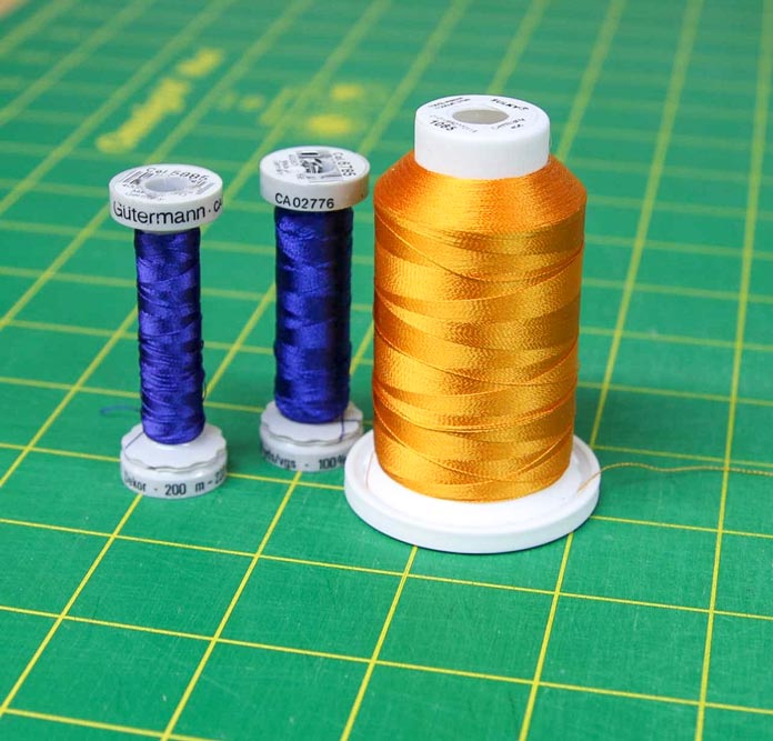 Two small spools of blue embroidery Gütermann thread and one big spool of gold embroidery thread; HUSQVARNA VIKING Designer Brilliance 80 sewing machine
