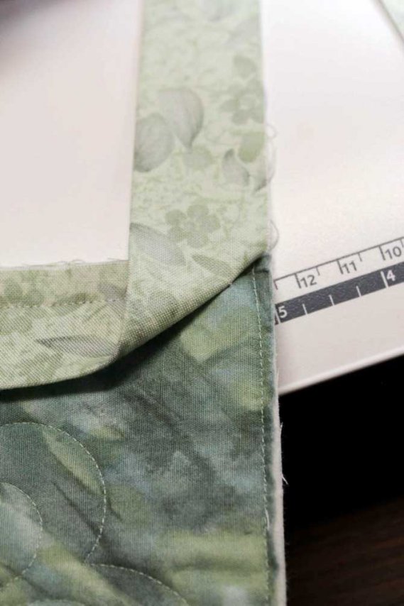 The binding strip is folded UP with raw edges parallel to the edge of the quilt. Notice how the binding strip is "just" pulling against the anchored seam.