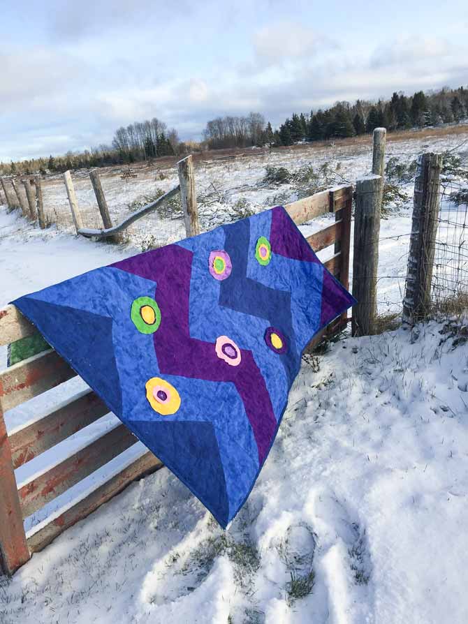 flannel quilt draped over wooden fence at farm.