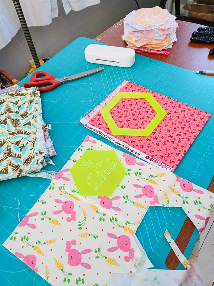  The pink flowered fabric is show with the large hexie (backing and border) ready to cut. The bunny and carrot fabric is shown with the smaller hexie (center of the bordered hexie). These are laid out on the cutting mat.  