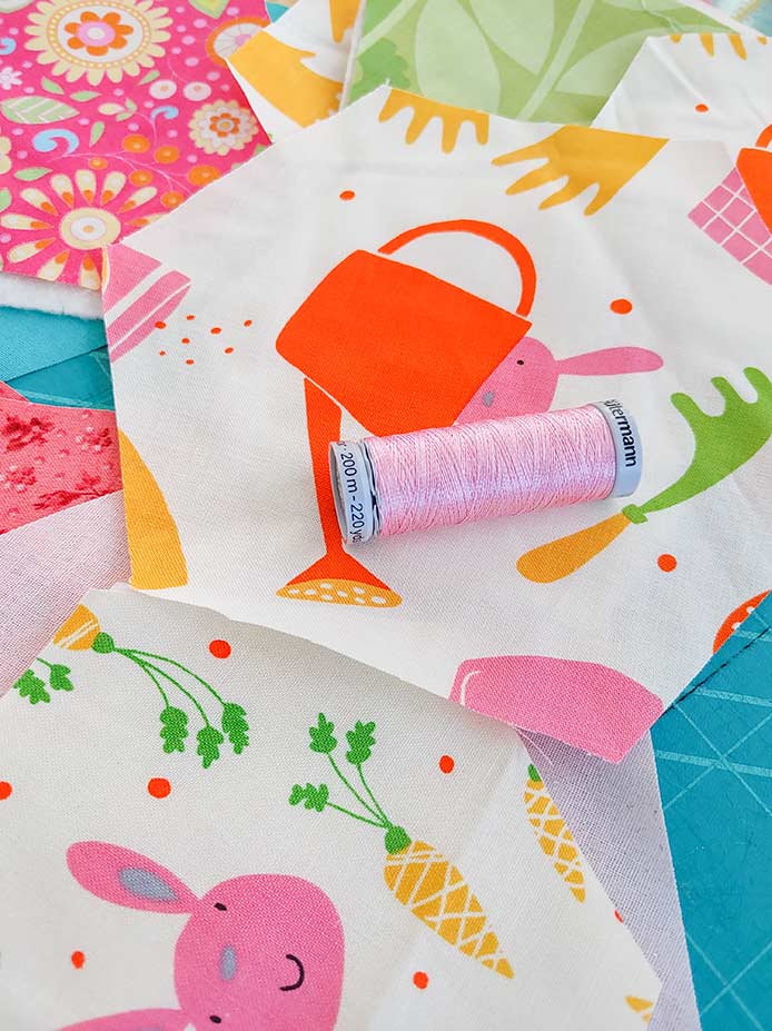 The pink topstitching thread is shown on the two types of bunny fabric with pink floral fabrics in the background. The thread will be used to top stitch the edges of these hexies.  