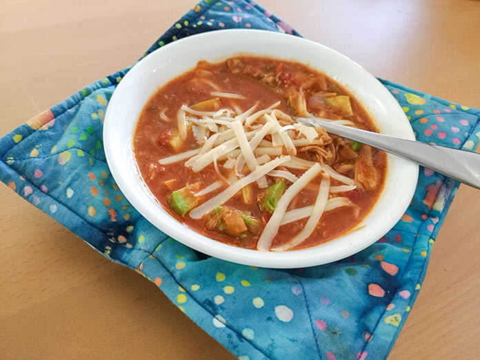 A yummy bowl of soup nestled in a quilted bowl cozy