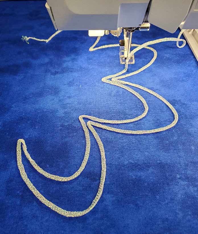 White yarn stitched on blue fabric for a Yarn Couching embroidery design on the Husqvarna Viking Designer Brilliance 80