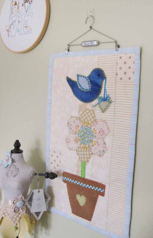 A hanger by Tim Holtz displays the studio bird mini quilt on a wall. WonderFil Specialty Threads.