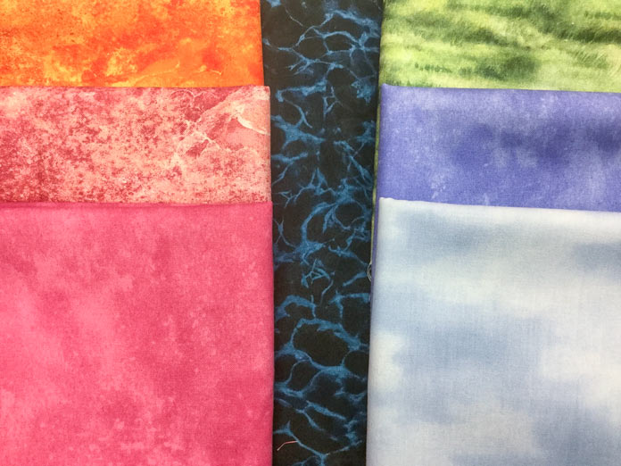  A selection of fabrics from Northcott including a light blue sky print, green grass print, a coral pink, a periwinkle blue, an orange ombre, a coral ombre and a dark blue crackle print  Northcott