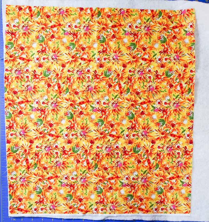 floral print in yellow, green and red on a piece of batting and blue cutting mat