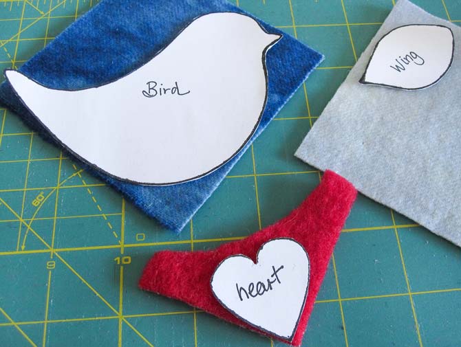 Templates of a bird shape, wing shape, and heart shape placed on wool pieces arranged on a cutting board. WonderFil Specialty Threads.