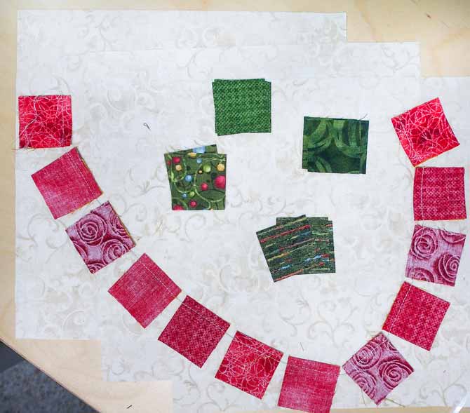 Red squares lying on cream fabric in a chain and green squares sitting above them