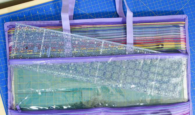 6 ½″ x 24″ ruler sliding into the clear zippered pocket of the purple mesh sunshine mat tote on a blue Unique mat