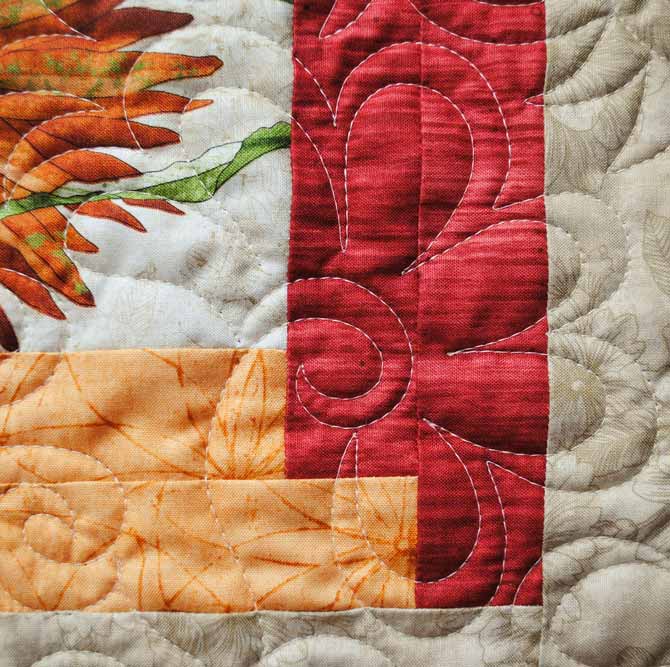 A close up of the flower design machine quilted with WonderFil's Master Quilter thread on the bedrunner made with Northcott's Artisan Spirit - Euphoria fabric.