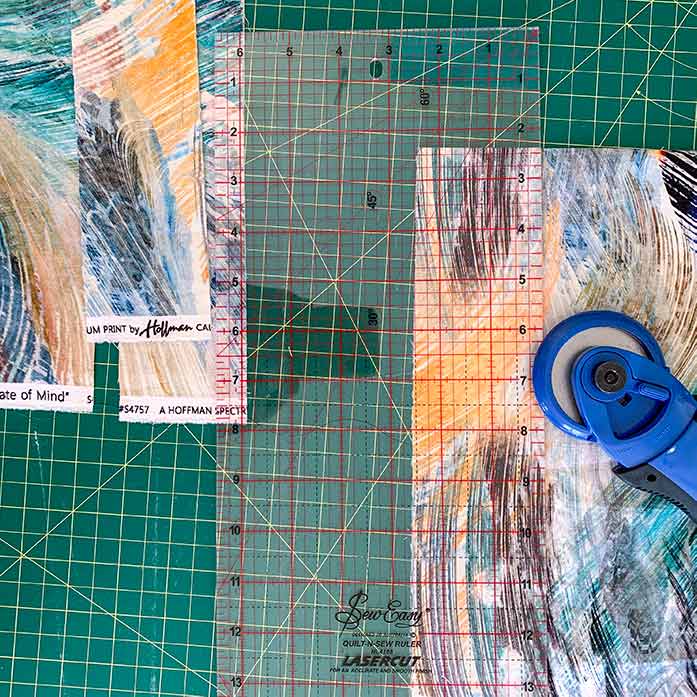 A picture showing a rotary cutter, acrylic ruler, self-healing cutting mat and patterned fabric