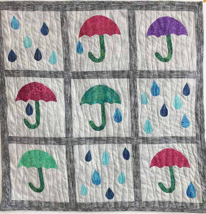 Completed umbrellas and raindrops quilted wall hanging, machine quilted with wavy lines. Northcott’s Artisan Spirit Shimmer Echoes.