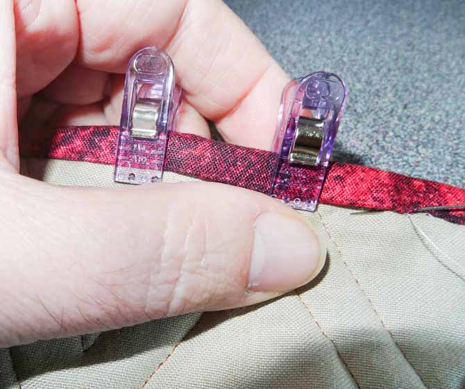 A close up picture showing the the hand sewing of the binging to the quilt. The binding i being held down by using Clever clips.