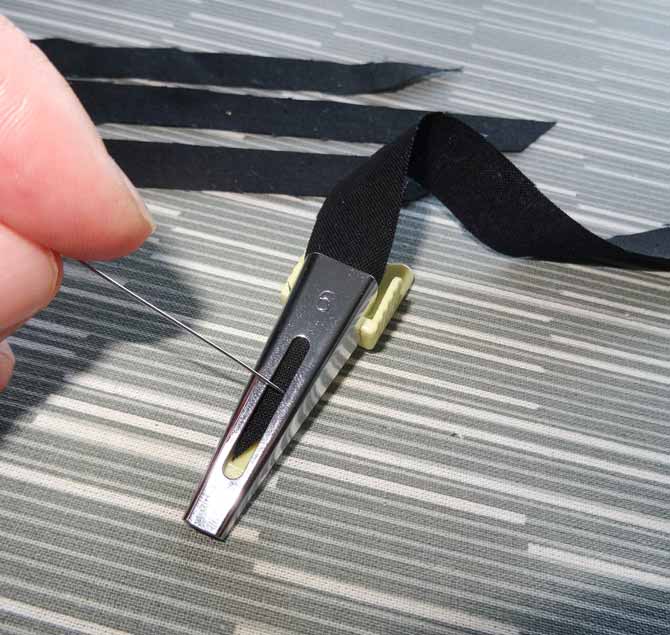 A pin is used to help guide a strip of black fabric through the Heirloom bias tape maker.