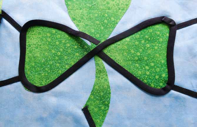 The black bias tape curves along the edge of two of the clover leaves and the raw end is tucked under another section of bias tape before it is fused with the iron.