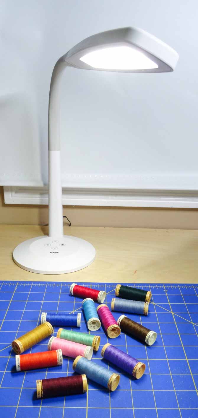 The SURElight M4T LED Desk Lamp on a desk top lighting several spools of coloful threads.