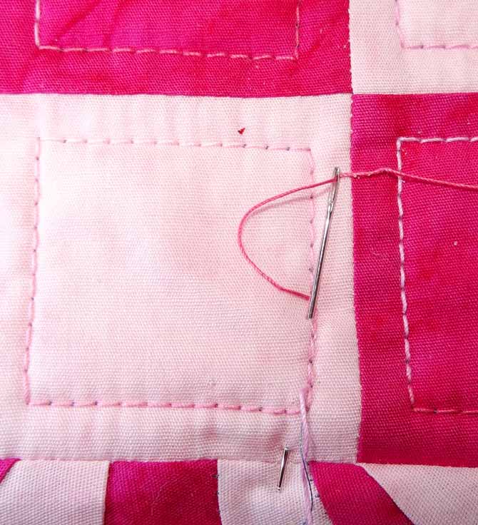 A sewing needed is used to bury a loose thread under the machine quilting on a quilt block. WonderFil DecoBob Prewound Bobbins.