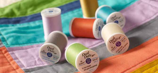 Spools of colorful Coats Dual Duty XP threads on a quilt