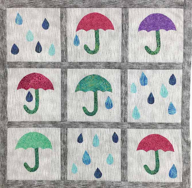 Umbrellas and raindrops against a light gray background completed quilt top with dark gray sashing and borders. Northcott’s Artisan Spirit Shimmer Echoes.