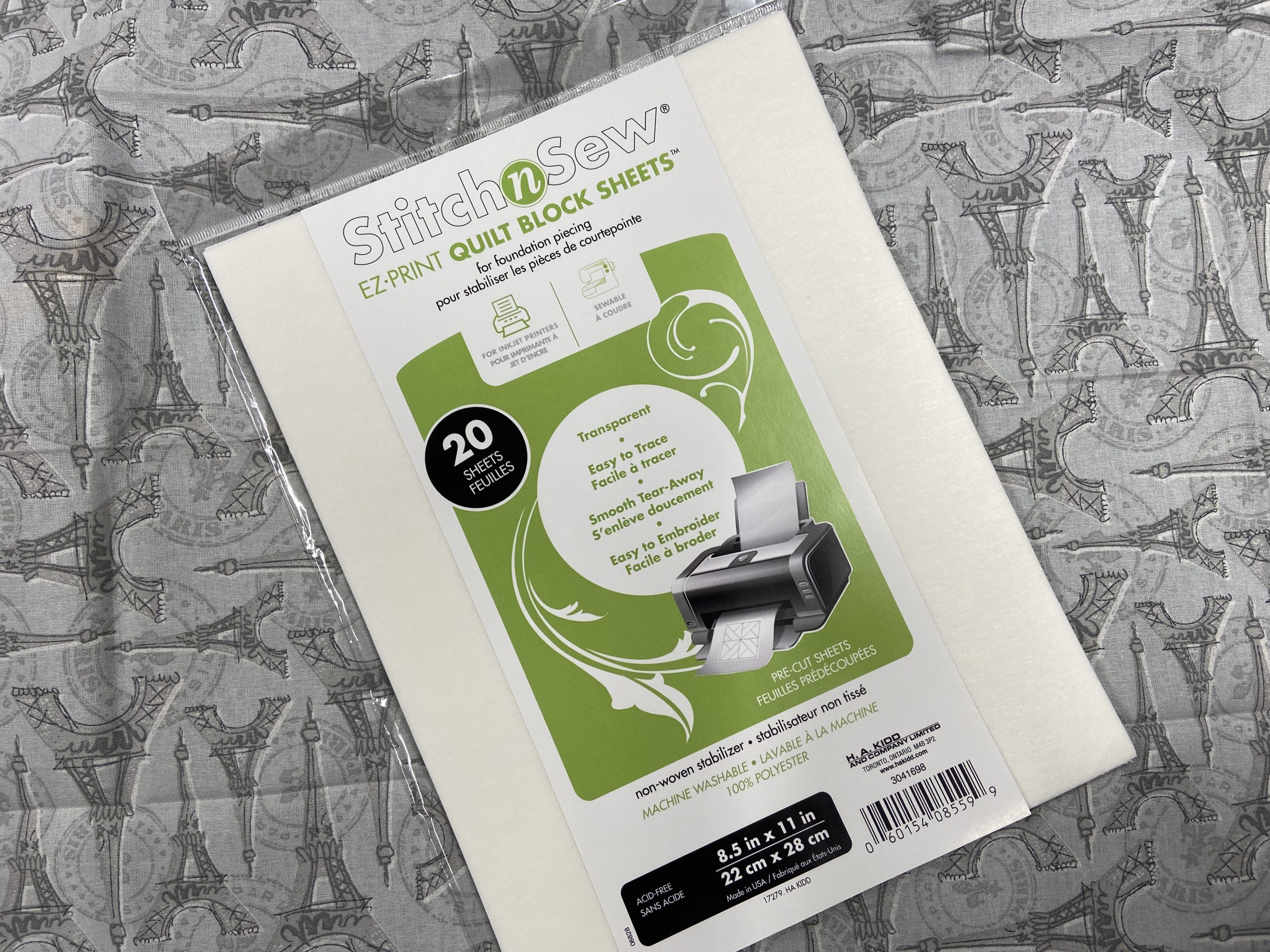 A white and green package of StitchnSew EZ Print Quilt Block Sheets sits on top of some gray Eiffel tower fabric.