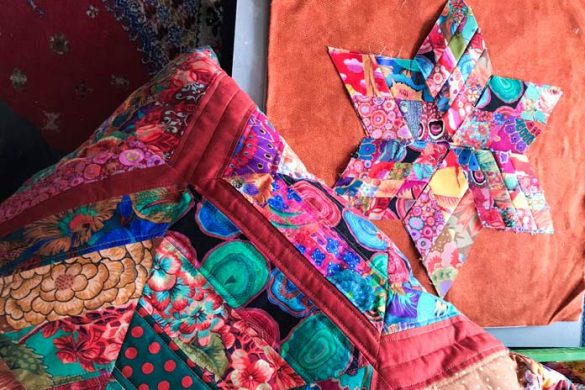 A close-up of a hexagon pillow in the bottom left-hand corner with a pieced star made of 4-patch diamonds on the top right-hand corner. All in bright and vibrant colors.