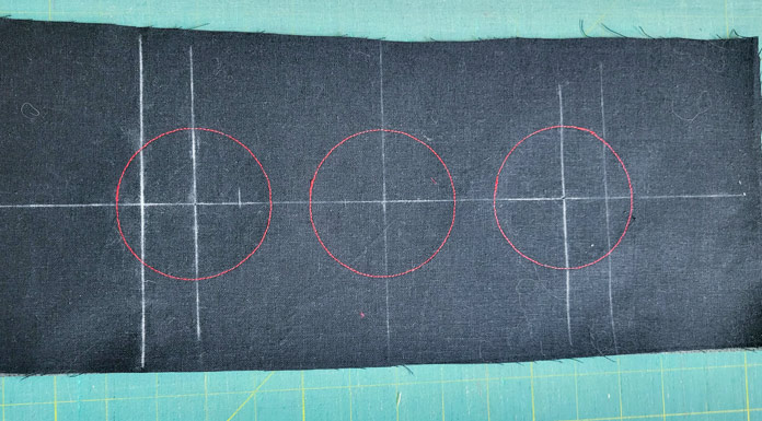 Circles of red stitching, with white reference marks on black fabric