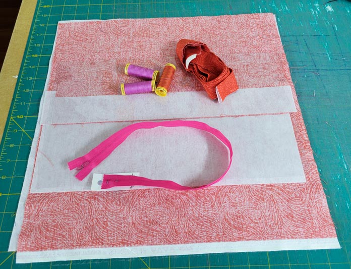 Orange and white fabric pieces, spools of thread, and a pink zipper ready to sew into a project bag using the Husqvarna VIKING ONXY 25