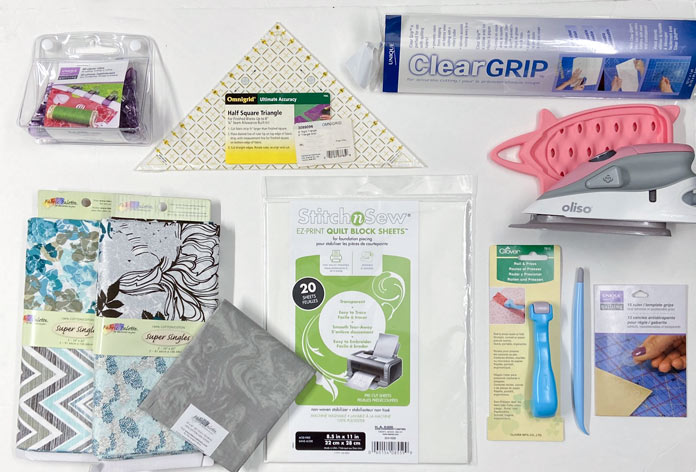 An assortment of quilting and sewing supplies on a table. UNIQUE Clear Grip, UNIQUE quilting Ruler/Template Grips, Omnigrid Ruler, Omnigrid Triangle Ruler, Fabric Creations Fabric Palette Pre-Cut Fabrics, Fairfield Crafter’s Choice Pillow Form