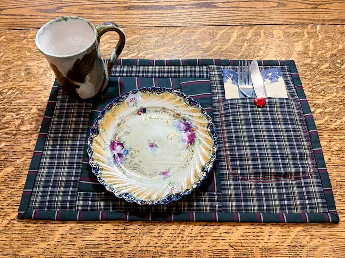 Placemat made from shirt fabric with pocket for a napkin and cutlery; OMNIGRIP Ruler 8½" x 8½", OLFA 45 mm Ergonomic Rotary Cutter, OLFA Endurance Rotary Blades, Sulky Tear-Easy stabilizer, Odif 505 Adhesive Fabric Spray, OLISO PRO TG1600 Pro Plus Smart Iron, Mary Ellen’s Best Press, Best Press Spray and Misting Bottle