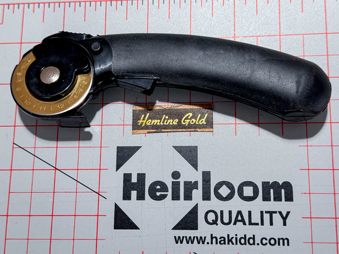 A Hemline Gold 45mm Rotary Cutter is placed on a gray Heirloom double-sided cutting mat.