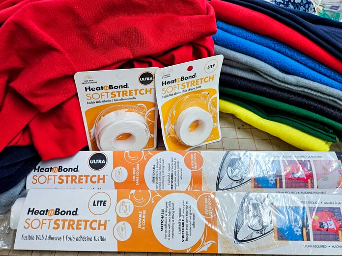 Gold and white packaging and colored fabrics; Learn how to use HeatnBond SOFTSTRETCH fusible web on knits, denim, fleece, and more