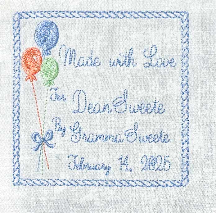 White fabric square with a blue rope like square border embroidered around the edge, green, orange, blue balloons on the left. Writing on the right saying who the quilt was made for, by whom and when; PFAFF creative expect 350, sewing machine reviews, mySewnet Quilting Software, mini quilt finishing, beginner quilting tips, quilt binding guide, machine quilting techniques, organic quilting, embroidery quilt labels, diy quilt projects, free motion quilting, free quilting project, free quilting patterns, baby quilt, free quilting tutorials