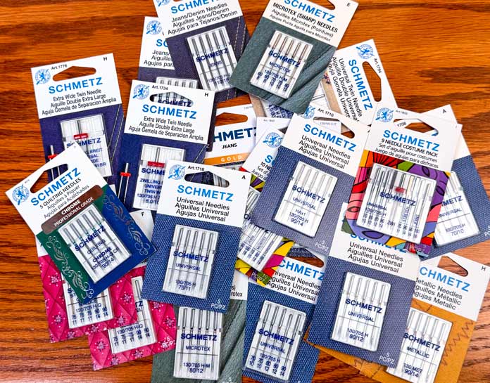 Multiple packages of different SCHMETZ sewing machine needles and sizes.