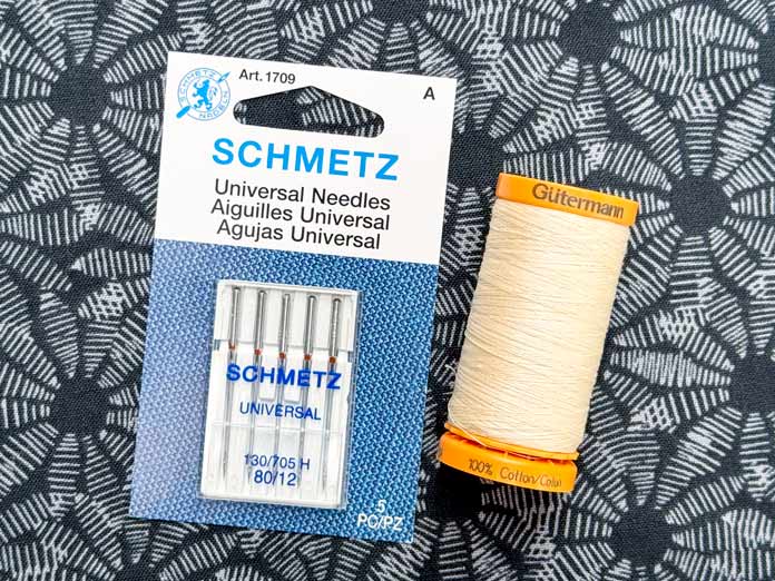A spool of Gütermann Cotton ivory 50wt Thread and a card SCHMETZ Universal Needles 80/12
