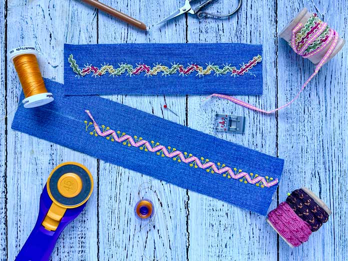 Two stitched ribbon samples on denim created using the PFAFF creative icon 2. The left sample features Single Ribbon Stitch #8 stitched with narrow variegated ribbon. The right sample showcases a decorative zigzag stitch (Stitch #2) paired with layered 3mm ribbons and yellow accent thread. Also pictured: 2A Fancy Stitch Foot, rotary cutter, Mettler 40wt polyester thread, scissors, marking pencil, and decorative ribbon spools. All materials are arranged on a white rustic wood background.