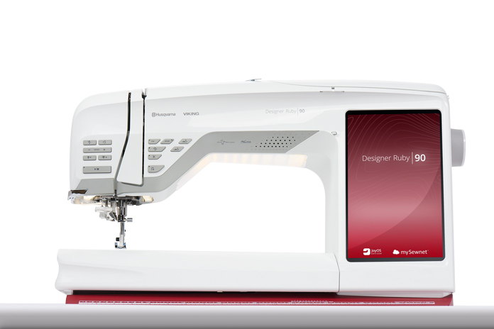A white sewing machine with a red touch screen; Husqvarna Viking Designer Ruby 90 sewing and embroidery machine, Inspira Fusible Fleece, Omnigrip 20½" square ruler, Singer 20 Steam Garment Press
