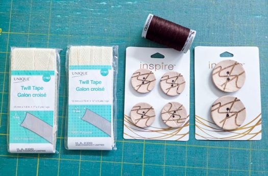 Two packages of twill tape, six buttons, and a spool of brown thread