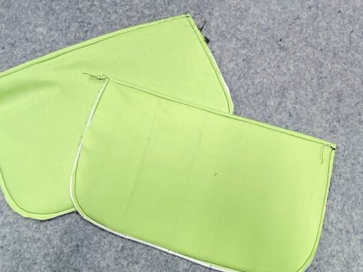 Two pockets lay on top of a grey pressing mat. The green lining and the basting stitch around the outside edge are visible.