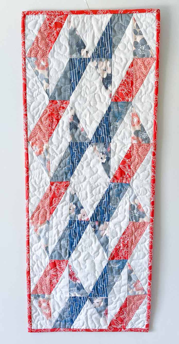 A red, white and blue table runner made with Half Rectangle Triangles. SCHMETZ Quilting needles, UNIQUE Sewing Fast Fade Fabric Markers, Omnigrid Rulers, OLFA Rotary Cutter, Komfort Kut Rotating Cutting mat, Fabric Creations Cotton Fabric.