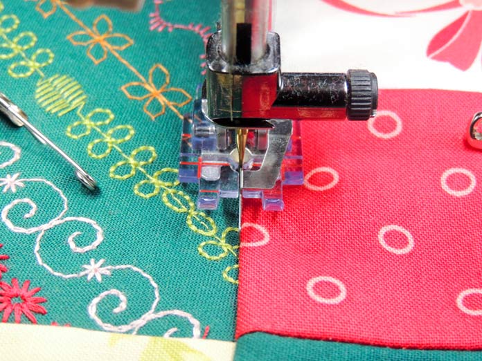 Clear Stitch-in-the-Ditch Foot for IDT System sewing in the ditch between the red fabric of a nine-patch and green stitched background fabric.