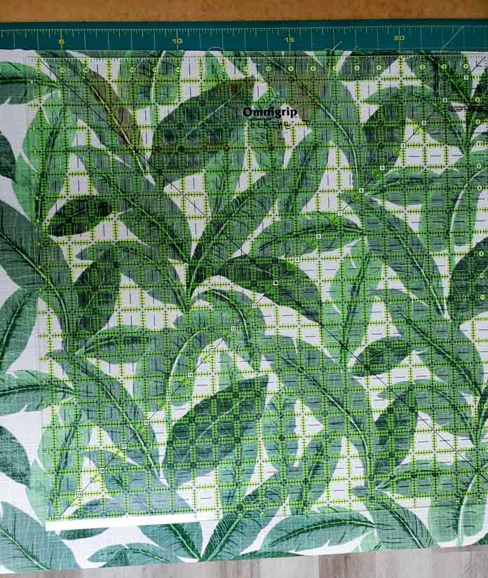 A green and white fabric with leaves under a quilting ruler
