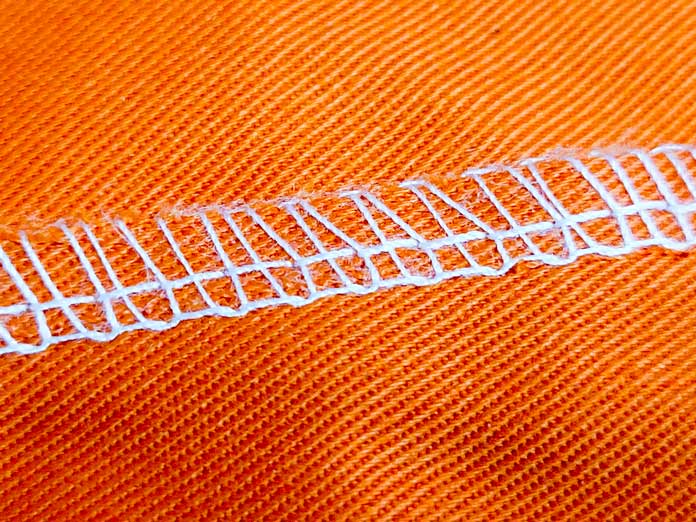 A serged seam with white fabric on orange fabric