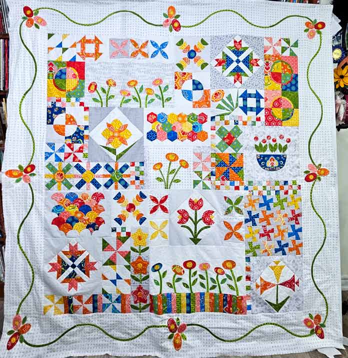 A white quilt top with blue, green, pink, and yellow pieces and a green vine on the border; the Husqvarna VIKING DESIGNER EPIC 3