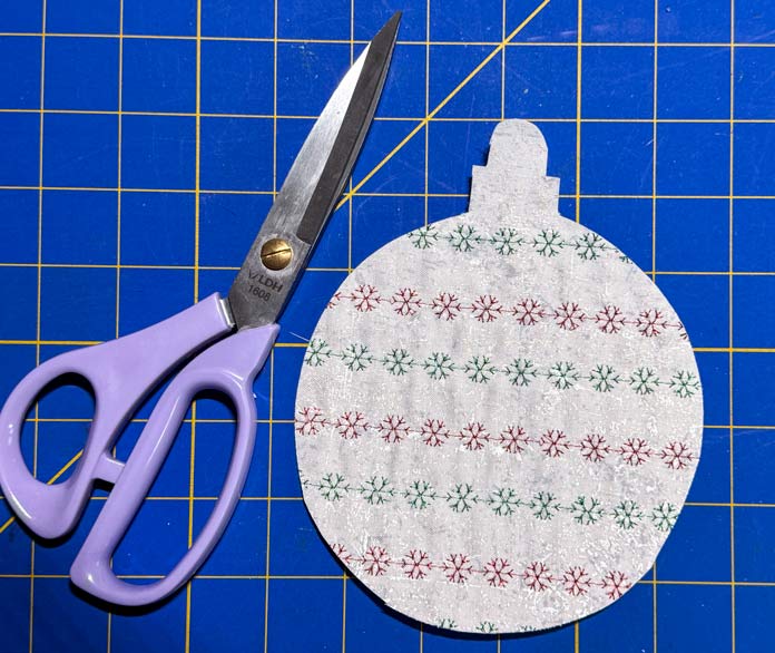 A pair of LDH purple scissors is beside a round ornament shape. 