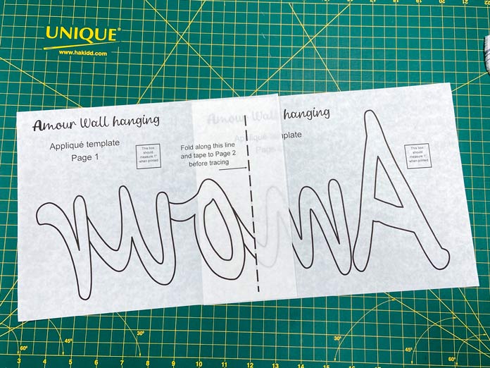 Two sheets of fusible web with the word Amour printed backwards on them sit on top of a green cutting mat.