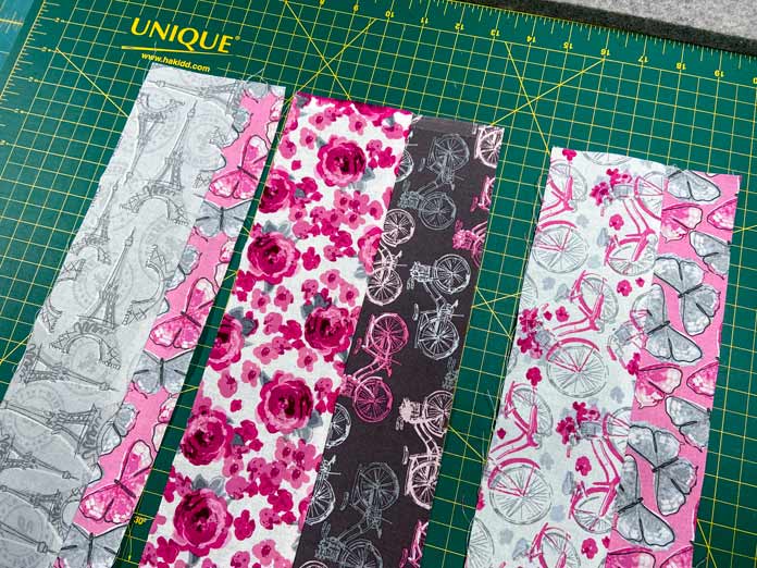 Three different pairs of fabric strips sit on a green cutting mat. The fabric prints range from white and pink, to gray, brown and pink.