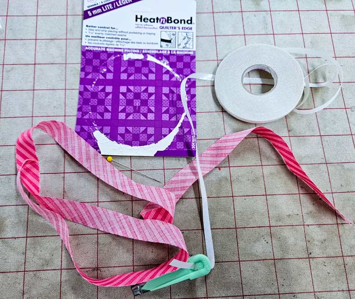 Pink fabric strip, HeatnBond Lite packaging, green Clover bias tape maker; HeatnBond Lite, fusible bias, Clover bias tape maker, sewing supplies.