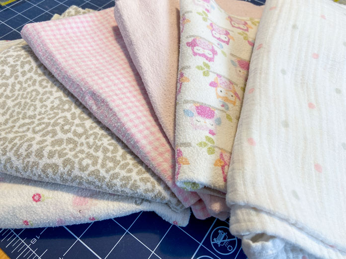 Six different receiving blankets with cute pink and gray designs sit on top of a blue cutting mat.