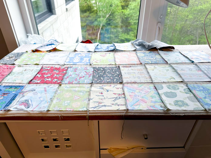 On a big ironing board, rows of 5” squares stitched together, ready for the seams to be pressed in the correct direction for piecing the rows together.