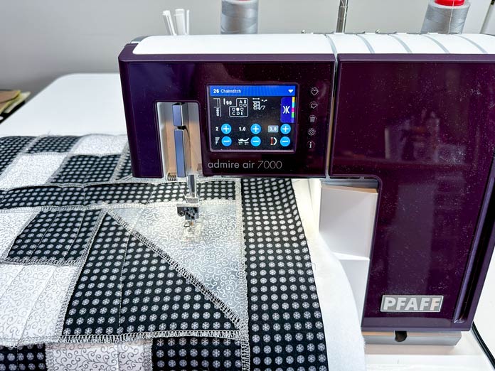 A burgundy and white serger chain stitch quilting a gray, black, white pieced runner with exposed seams.